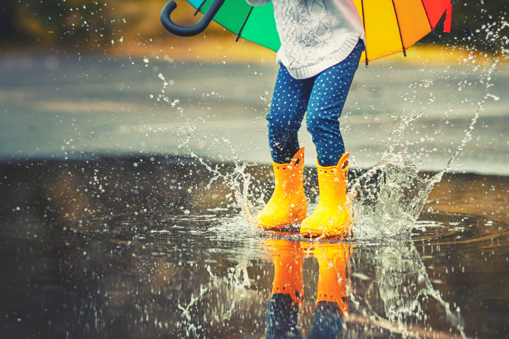 Feet of child in yellow rubber boots jumping over a puddle in the rain